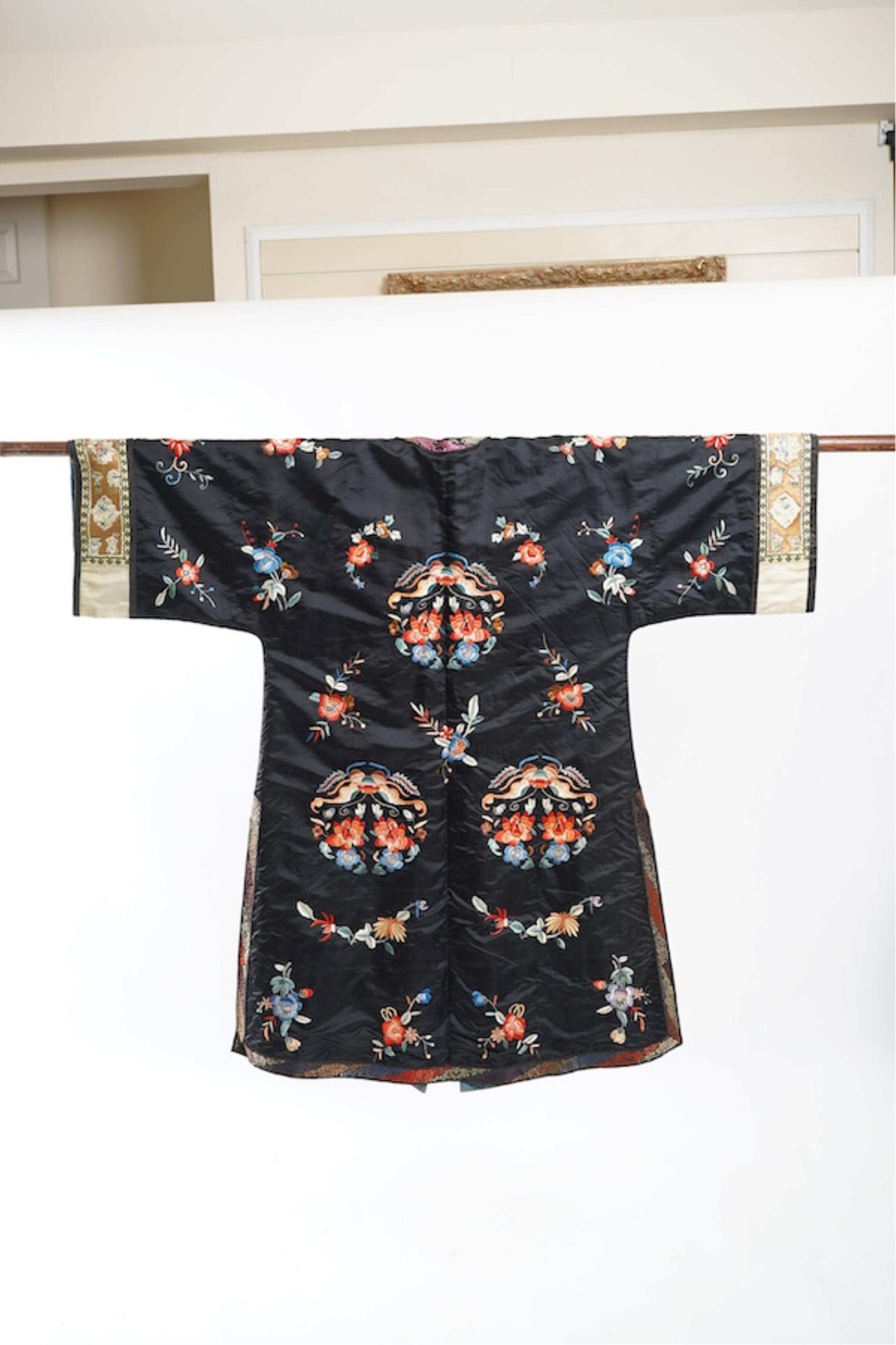A late 19th early 20th century Chinese black silk polychrome embroidered ladies robe, decorated with cream silk, gilt and Peking knot bordered sleeve bands. The sleeve bands worked with fine figural and other embroidered